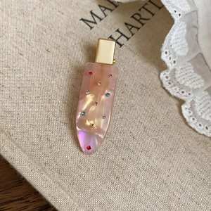 Macro detail of iridescent drop hair clip with colorful rhinestones on gold metal base