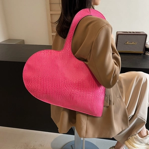 Pink heart-shaped tote bag with crocodile texture carried by model in a modern style
