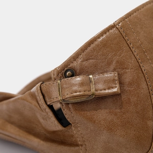 Macro detail of brown leather beret featuring retro metal buckle and stitching