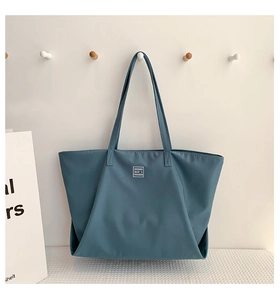 Detail of blue nylon tote bag with white minimalist label and folded side structure