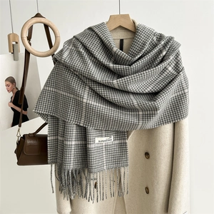 Detail eines grauen Schals mit Hahnentrittmuster, Fransen und Textiletikett