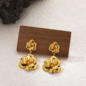 Detail of 18K gold camellia flower earrings with polished 3D petals on a dark stone