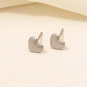 Close-up of silver heart stud earrings with dotted texture on beige fabric background