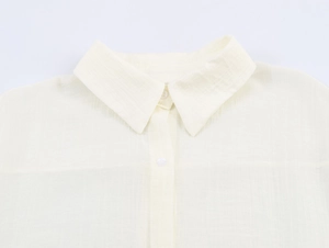 Detail of off-white linen shirt collar with textured fabric and white button closure