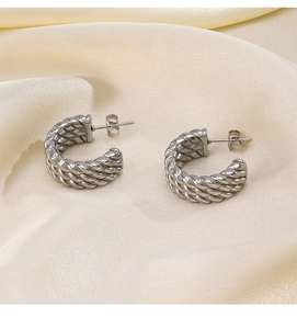 Macro view of silver-tone twisted rope earrings on soft yellow silk fabric background