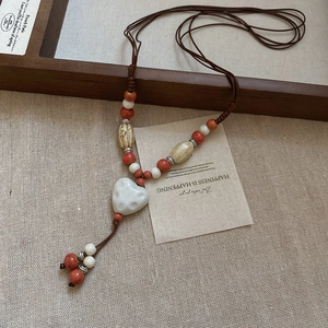 Détail d'un collier pendentif cœur en céramique vintage avec cordon tissé et perles colorées