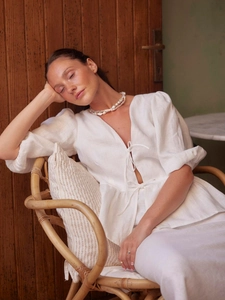 Detail of white cotton v-neck top with bow ties, puff sleeves and pearl necklace
