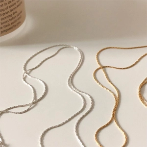 Detail of minimalist gold and silver link chains on a clean beige background