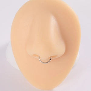 Close-up of a polished silver nose ring displayed on a realistic silicone nose model