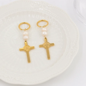 Détail de boucles d'oreilles croix dorées avec perles et relief religieux sur plat blanc