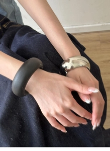 Detail of chunky polished silver and matte black wide dome bangles on a woman's wrist