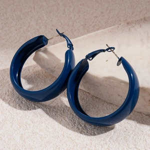 Détail de grandes boucles d'oreilles créoles géométriques bleu foncé mat sur pierre