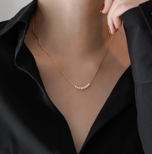 Detail of minimalist titanium steel gold necklace with eight elegant white pearls