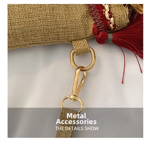 Macro detail of the golden lobster clasp and red tassel on a woven straw envelope clutch