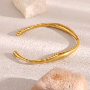 Detailed view of an 18K gold plated stainless steel bracelet with an irregular wave design