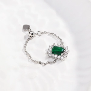 Detail of adjustable chain ring with emerald-cut green stone and silver heart charm