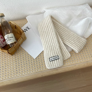 Detail of cream knit scarf featuring vertical ribbed texture and a woven brand label