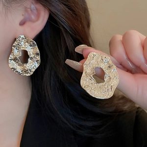 Detail of gold-tone irregular hollow metal earrings with hammered texture on ear