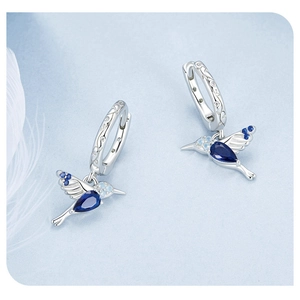 Macro shot of hummingbird earrings with blue gemstones and white feathers on the background