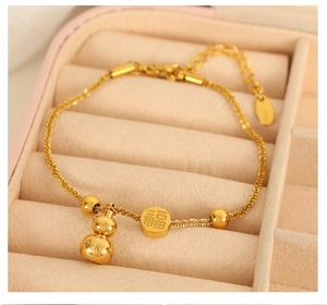 Macro detail of gold stainless steel bracelet with gourd charm and fu character pendant