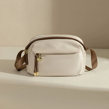 Close-up of cream shoulder bag with dark brown strap and golden zipper pendant