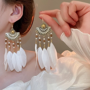 Close-up of bohemian style earrings featuring white feathers and antique bronze beads