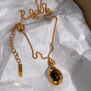 Detail of 18k gold plated necklace with oval tiger eye pendant on white wrinkled paper
