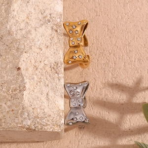 Close-up of gold and silver bow-shaped ear cuffs with star patterns on natural stone