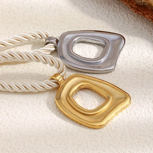 Detail von quadratischen Hohl-Anhängern in Gold und Silber an weißer Kordelkette