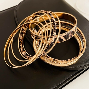 Detail of gold metal bracelets set with leopard print fabric wrap on black leather background