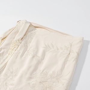 Détail de la broderie florale crème et des pompons tressés sur une jupe courte