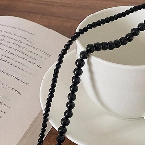 Minimalist black agate bead necklace displayed on a white coffee cup over an open book