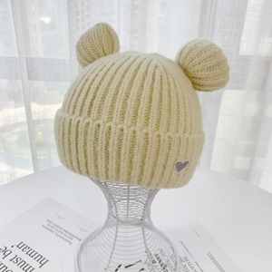 Detail of soft yellow knit beanie with ear pom-poms and a sparkly gray heart patch