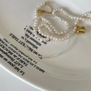 Minimalist S925 silver open bangle and gold heart pearl necklace on white ceramic tray