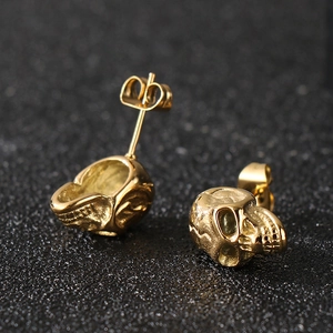 Macro shot of gold skull stud earrings featuring fine detail and polished steel finish