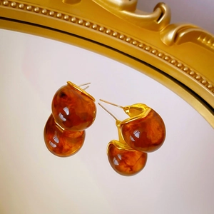 Détail de boucles d'oreilles en résine ambrée avec bords dorés sur miroir rétro