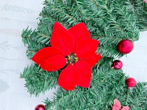 Close-up of green PVC Christmas garland with red velvet poinsettias and ornaments