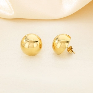 Detail of minimalist gold-plated semi-sphere stud earrings on soft fabric background