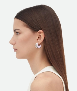 Close-up of C-shape earrings with pink enamel and silver finish on a female model