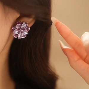 Détail macro de boucles d'oreilles fleurs en résine violette nacrée sur un modèle