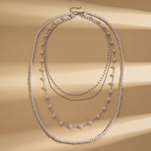 Macro detail of multi-layer faux pearl necklace with silver-tone metal chains on texture