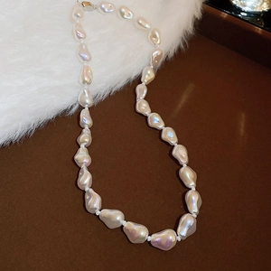 Close-up of white baroque pearl necklace with silver clasp on deep brown tray