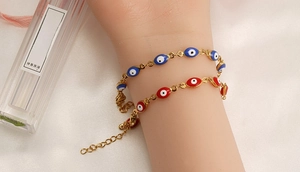 Close-up of gold chain bracelets featuring colorful evil eye charms and lobster clasp