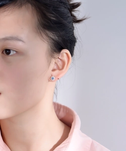 Detailed view of flower stud earring with blue gemstone and pearl petals worn on ear
