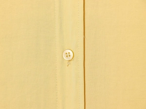 Detail of yellow poplin shirt showing fine cotton texture and pearl button fastening