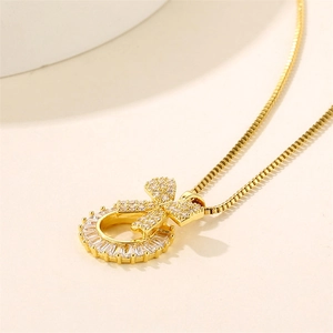 Golden stainless steel bow necklace with round clear zircon pendant on beige background