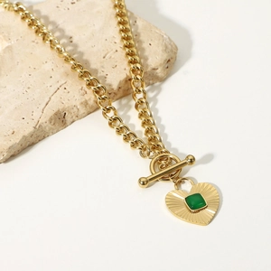 Detail of heart pendant necklace with green gemstone on a natural stone background