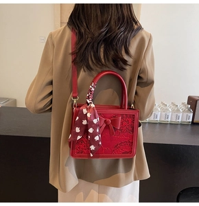 Detail view of red bridal handbag with embroidery, silk scarf handle, and bow ornament