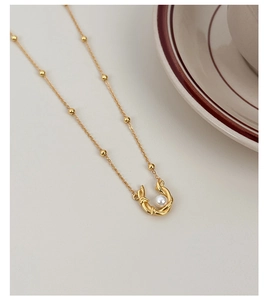 Detail of s925 silver pearl necklace featuring a horseshoe pendant on a gold beaded chain