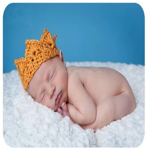 Nahaufnahme eines Babys mit gelber Strickkrone auf einer weichen weißen Kunstfelldecke